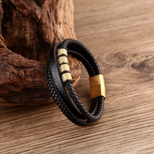 Detail of multilayer black braided leather bracelet with golden knurled metal cylinders
