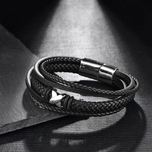 Detailed macro of men's multi-layer braided leather bracelet on dark textured rock surface