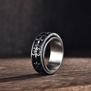 Anello rotante in acciaio inossidabile con rilievi fleur-de-lis su fondo in legno scuro