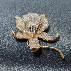 Elegant gold lily flower brooch with white zircons and pear-cut main stone on black background