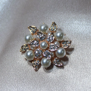 Detail of flower brooch with white pearls and sparkling crystals on golden base