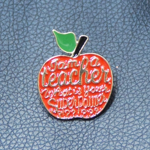 Close-up of red apple teacher enamel pin on blue leather with superpower text