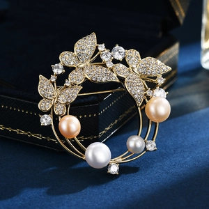 Elegante broche corona dorada con mariposas de cristal y perlas junto a un joyero
