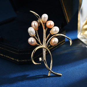 Spilla orchidea dorata con perle bianche rosa e champagne su sfondo di velluto