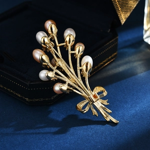 Elegante spilla a bouquet dorata con perle d'acqua dolce su fondo di velluto scuro