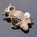 Elegant owl brooch with sparkling crystals and a white pearl on a golden metal base