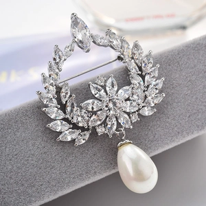 Detailed close-up of zircon wreath brooch with white teardrop pearl on velvet stand