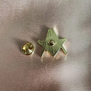 Golden Freemasonry symbol brooch pin with vertical metal texture on rose gold satin fabric