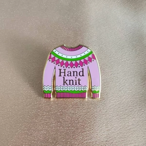 Détail d'une broche en émail rose style pull tricoté sur fond de velours champagne
