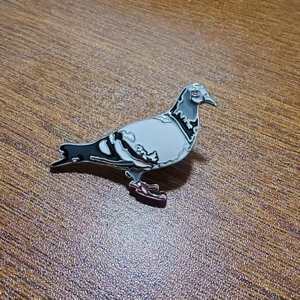 Detailed view of enamel pigeon brooch with grey and white finish on wood background