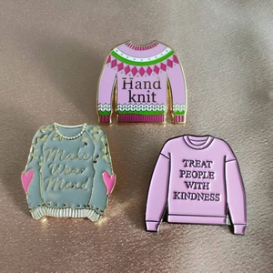 Détail de trois pin's en émail représentant des pulls en tricot et un slogan inspirant