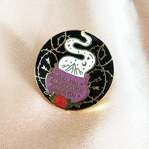Detail of round enamel brooch with purple cauldron and inspirational quote on pink silk