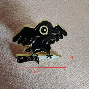 Detail view of a cartoon crow enamel pin with knife showing 3.1cm width and 6g weight