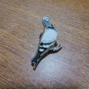 Close-up of pigeon enamel brooch with silver metal edges on a dark wooden surface
