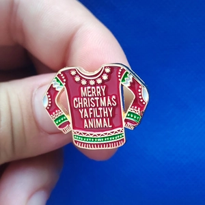 Christmas enamel pin shaped like a red ugly sweater with Merry Christmas text