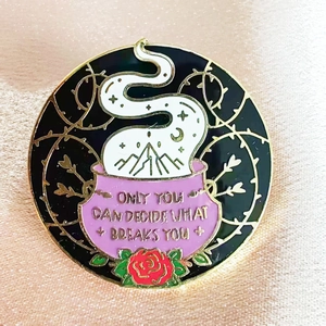 Detailed macro shot of an enamel pin featuring a pink cauldron and motivational quote