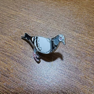 Minimalist pigeon enamel brooch with silver metal trim on a dark wood background
