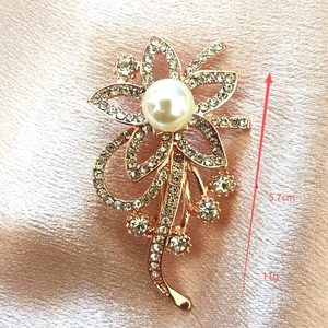 Detail van een elegante 5,7cm roségouden bloemenbroche met parel en glanzende strassteentjes