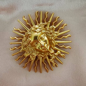 Close-up of golden sun goddess face brooch with vintage metallic rays on pink fabric