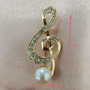 Detail view of a gold musical treble clef brooch with white crystals and pearl, 4.4cm tall