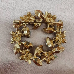 Back view of gold crystal floral wreath brooch showing metal pin clasp on silk background