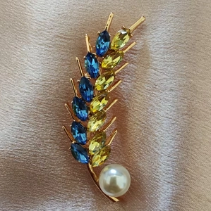 Macro detail of wheat brooch with blue crystals and large white pearl on pink silk