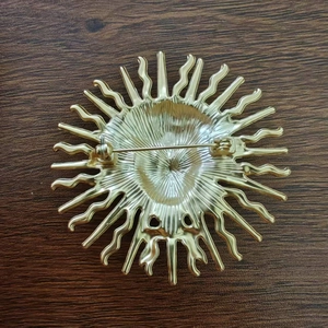 Golden sun goddess brooch in retro style shown with safety pin on wooden background