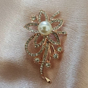 Gedetailleerd beeld van roségouden bloemspeld met fonkelende strass en witte parel