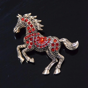 Running horse brooch in antique gold finish with red rhinestones on a dark background