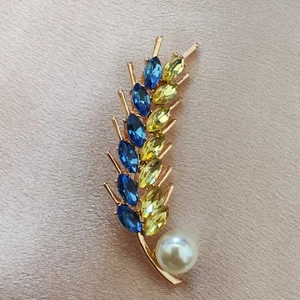 Elegant gold wheat brooch with blue and yellow crystals and a white pearl on satin