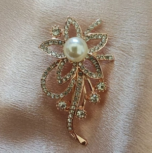 Detailopname van een roségouden bloembroche met strassteentjes en een centrale parel