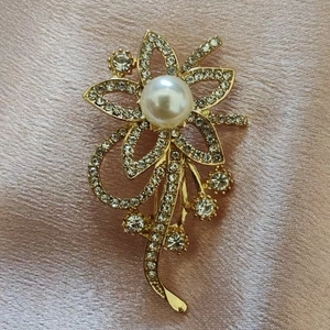 Detailopname van de gouden bloemenbroche met witte parel en fonkelende strass-stenen