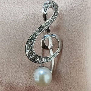 Elegant treble clef brooch with silver crystals and a white pearl on pink silk