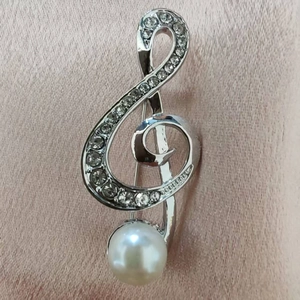 Macro detail of a musical G-clef brooch with sparkling rhinestones and a white pearl accent