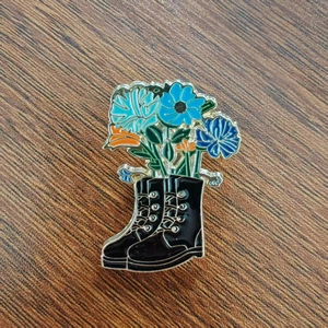 Dettaglio di una spilla smaltata con stivali neri e vivaci fiori blu su legno