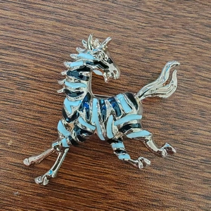 Elegante spilla a forma di cavallo dorata con smalto nero e blu in posa dinamica