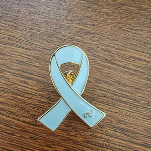 Light blue enamel awareness ribbon brooch with gold-plated metal edges on wood
