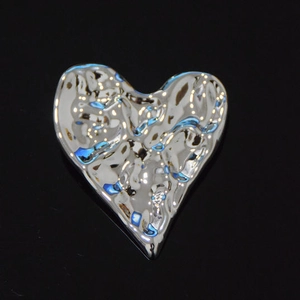 Détail macro d'une broche en forme de cœur avec texture argentée martelée sur fond noir