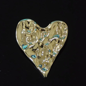 Détail d'une broche cœur dorée avec une texture métallique martelée au style liquide