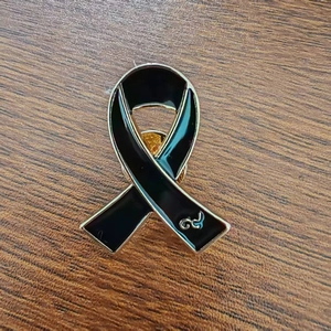 Black ribbon awareness brooch with golden edges and silver Thai number on wood surface