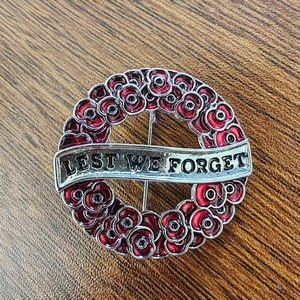 Poppy wreath brooch with Lest We Forget engraving in red enamel on a wooden surface