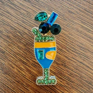 Creative cocktail glass enamel brooch with blue and green rhinestones on wood surface