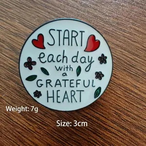 Round enamel brooch with 'Grateful Heart' quote and floral accents on wooden background