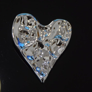 Détail macro d'une broche cœur argentée avec une texture métallique martelée ondulée