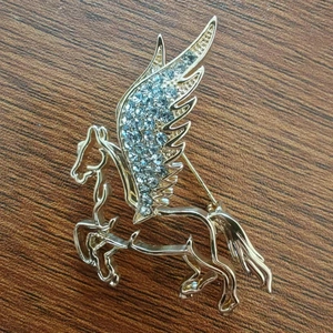 Golden Pegasus brooch with light blue rhinestones on a wooden background