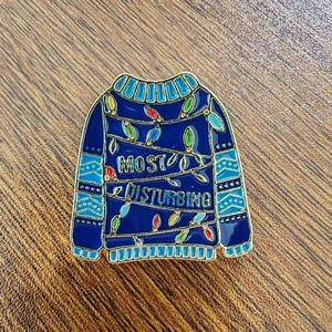 Blue Christmas sweater enamel brooch with festive light bulbs on a wooden background
