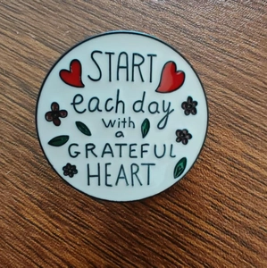 Enamel brooch with 'Start each day with a grateful heart' quote and red heart on wood background