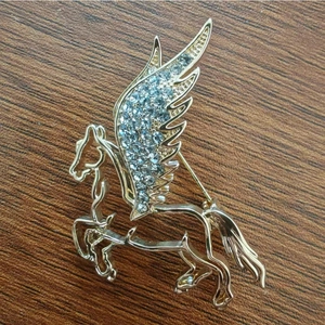 Close-up of golden pegasus brooch with sparkling rhinestones on dark wood surface