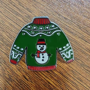 Detail of Christmas ugly sweater enamel pin with snowman and green metal finish