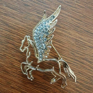 Macro detail of golden Pegasus brooch showing intricate wings with white rhinestones